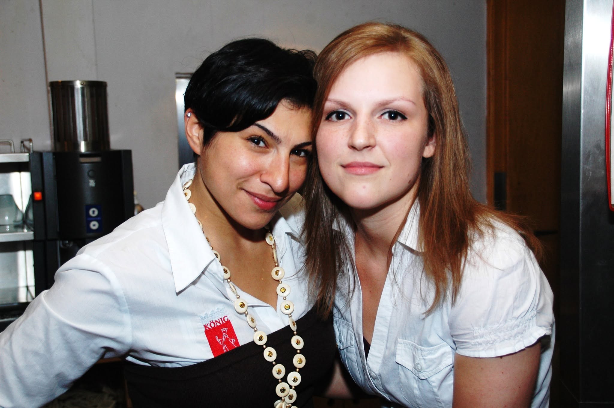 Zwei Personen in weißen Blusen posieren gemeinsam an der Bar.