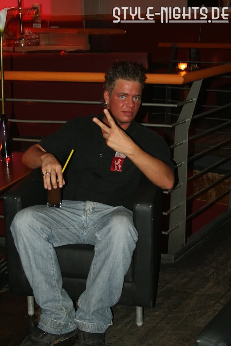 Eine Person im KÖNIG-Polo sitzt mit einem Getränk im Sessel und zeigt das Peace-Zeichen.