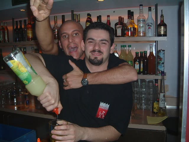 Zwei Personen posieren hinter der Bar mit einer Flasche und erhobenen Händen.